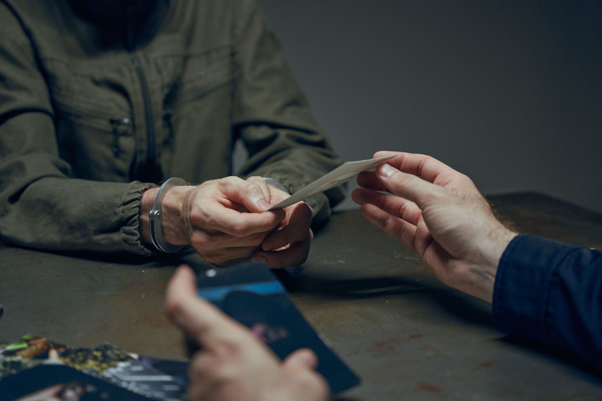 Hands exchanging evidence during an interrogation scene in a dimly lit room.